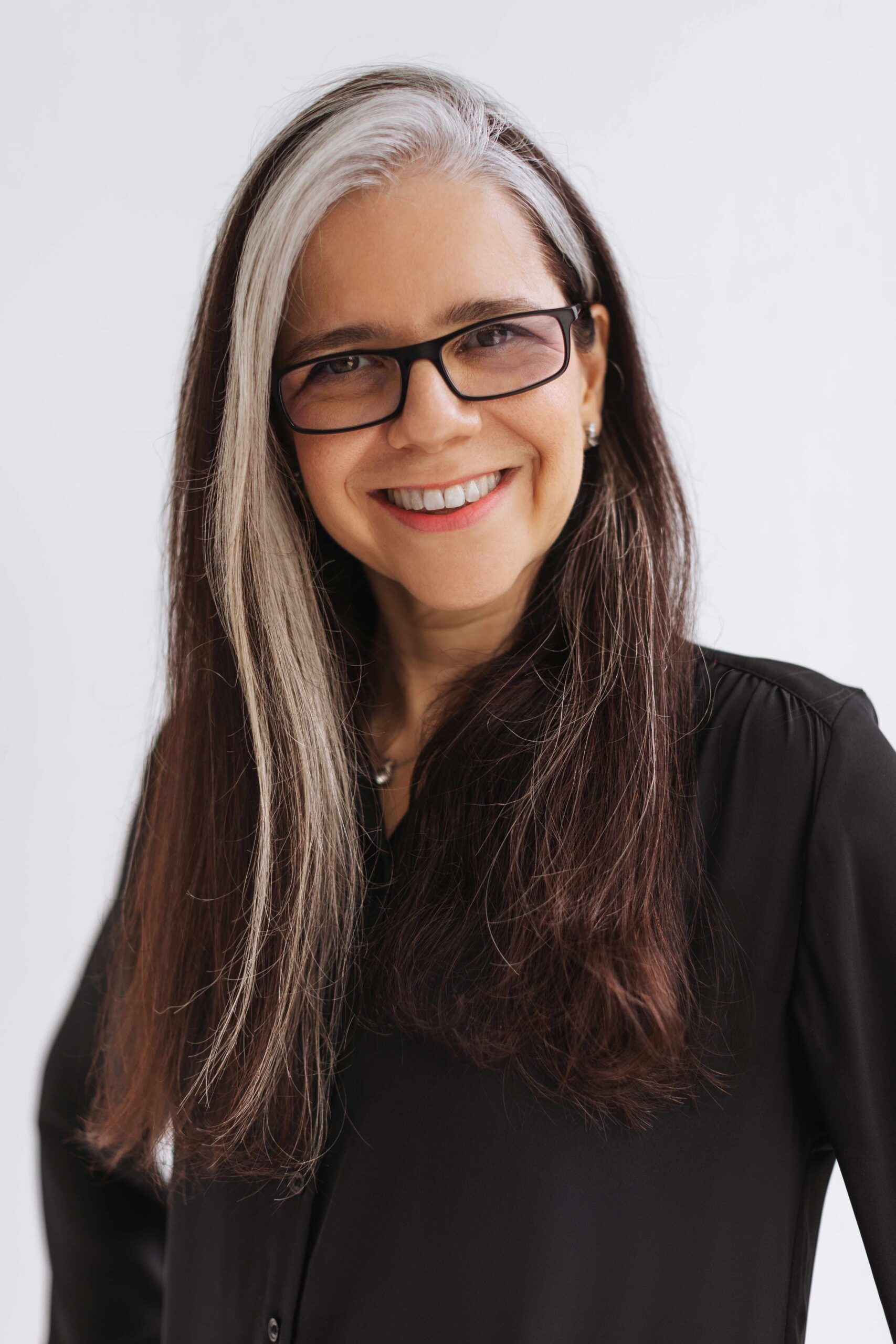 A middle-aged woman in black. Her hair is long with a stunning streak of white.